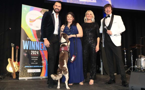 Alex accepts her award from TV presenter Rylan Clark, with Hearing dog Otto and two other hosts.